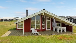 Een chalet met rode dakpannen, grote ramen, een terras en tuinmeubilair.