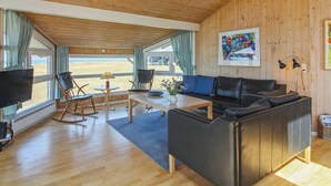 Een knusse woonkamer met een houten plafond, een zwarte leren bank, een houten salontafel en een televisie.