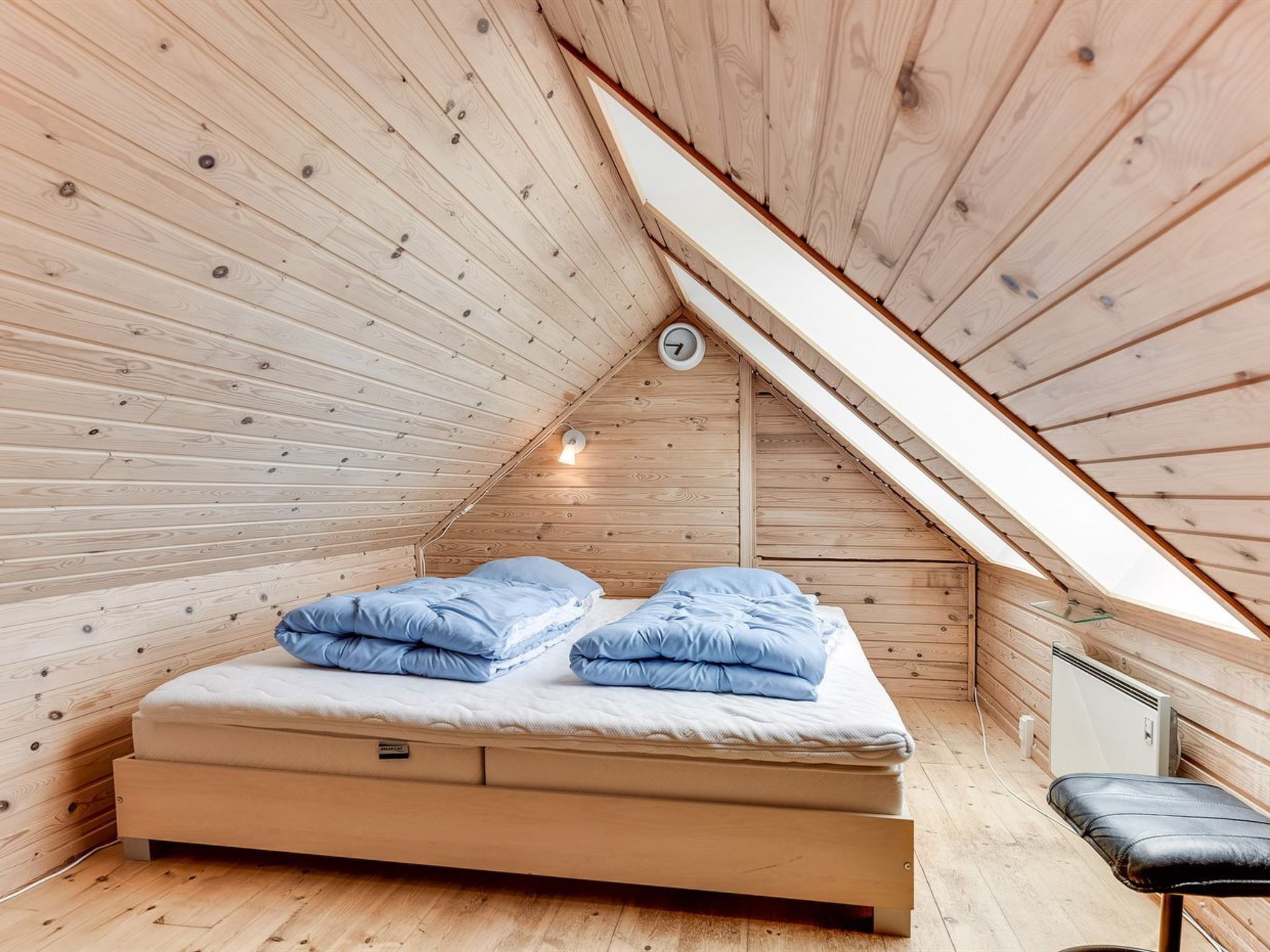 Una habitación pequeña de madera con techo inclinado, una cama, un banco y un calentador a la vista.