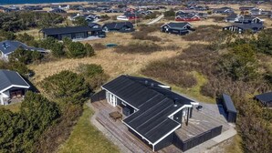 Une vue aérienne d’un quartier résidentiel avec des maisons, dont certaines ont des toits rouges, entouré d’un paysage naturel et offrant une vue sur la mer.