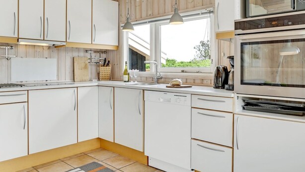 Une cuisine moderne avec des meubles blancs, un four encastré et une fenêtre qui laisse entrer la lumière naturelle.