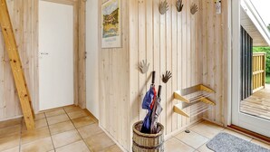 Un intérieur en bois avec une porte, un tableau encadré, des décorations faites à la main, un panier en osier contenant des parapluies et un banc en bois.