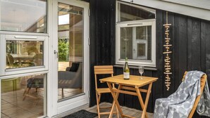 Une table et une chaise en bois sont placées à l’extérieur d’un bâtiment à la façade noire et aux ornements blancs.