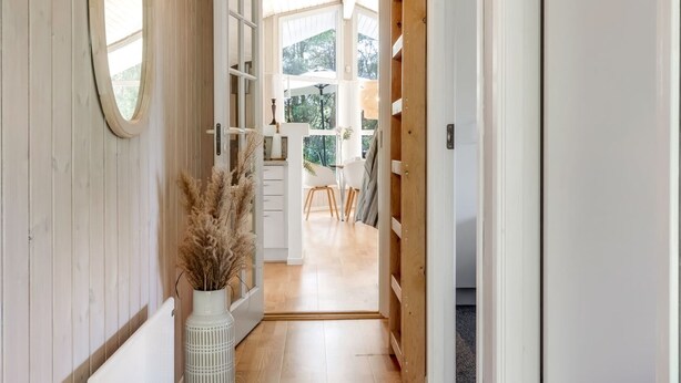 Een hal met houten wanden, een witte deur en zicht op een kamer met een tafel en stoelen.