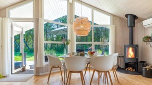Een modern interieur met een eethoek, grote ramen, een houtkachel en uitzicht op de omgeving.