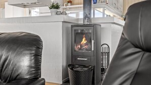 Un salon moderne avec un poêle à bois, des fauteuils en cuir et un plafond blanc.