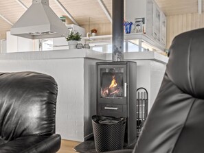 Un salon moderne avec un poêle à bois, des fauteuils en cuir et un plafond blanc.