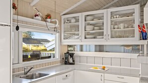 Une cuisine moderne avec des meubles blancs, un évier en acier inoxydable et une fenêtre donnant sur une maison.