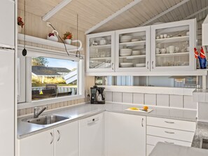 Une cuisine moderne avec des meubles blancs, un évier en acier inoxydable et une fenêtre donnant sur une maison.