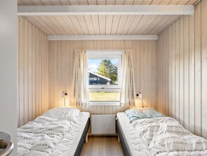 Une chambre avec deux lits, une fenêtre avec des rideaux et une vue sur un bâtiment à l’extérieur.