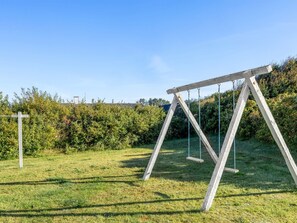 Une balançoire installée dans un espace herbeux, avec une haie en arrière-plan.