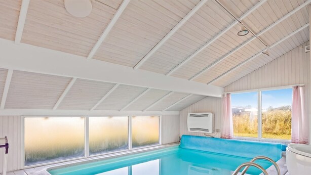 Une piscine intérieure avec des parois en verre transparent, un bord bleu et un escalier en métal.