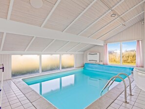 Una piscina interior amb parets de vidre transparent, vora blava i escala metàl·lica.
