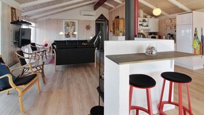 A spacious living area with a black sofa, wooden chairs, a TV, and a kitchen area with a refrigerator and bar stools. - "Skrallan" - 400m from the sea by Interhome (Hjørring)