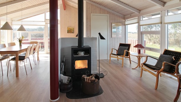 A spacious room with a large wooden ceiling, a central fireplace, and a dining area with chairs and a table. - "Skrallan" - 400m from the sea by Interhome (Hjørring)