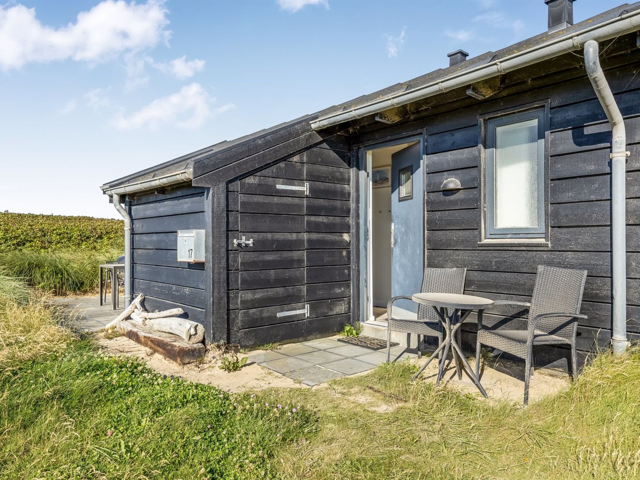 Eine Hütte mit Tür, Fenster und einer kleinen Sitzgelegenheit im Freien mit Tisch und zwei Stühlen.