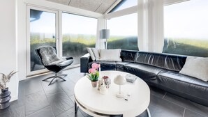 A modern living room with a black leather sofa, a round white coffee table, and a black chair. There is a large window providing a view of the outdoors. - "Antonie" - 95m from the sea by Interhome (Hjørring)