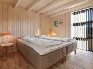 A bedroom with a wooden slat wall, a bed with white bedding, two bedside lamps, and a window with black and white striped blinds.