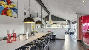 A modern kitchen with a long counter, pendant lights, and a red accent wall.