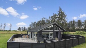 A modern house with a deck, large windows, and a covered outdoor seating area.
