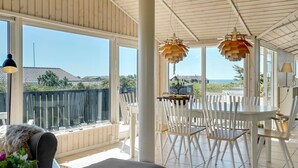 Una habitació àmplia amb grans finestres, zona de dinar amb caires blancs i vistes al mar.