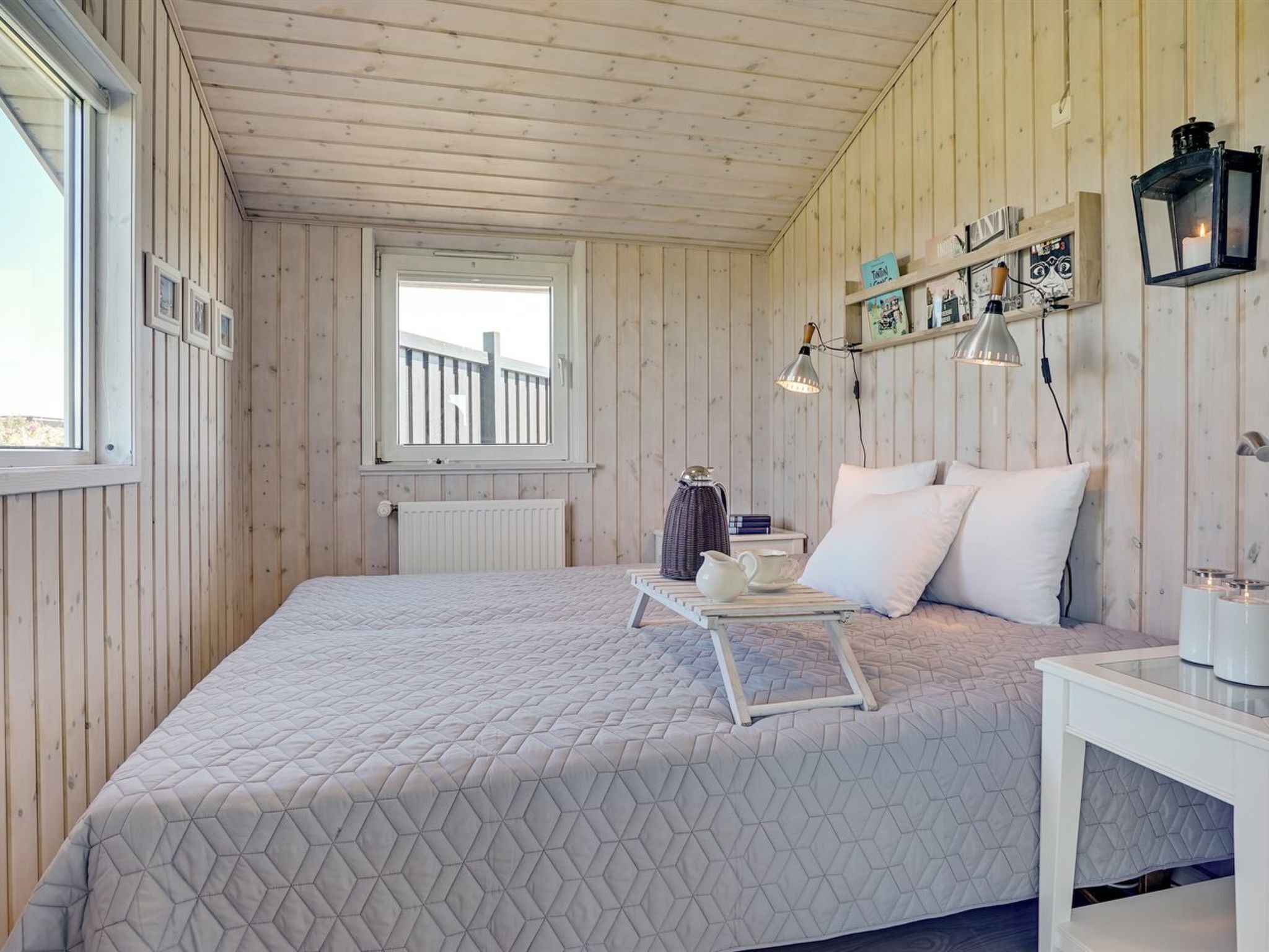 A bedroom with a bed, a bedside table, a window, and a view of the outside.