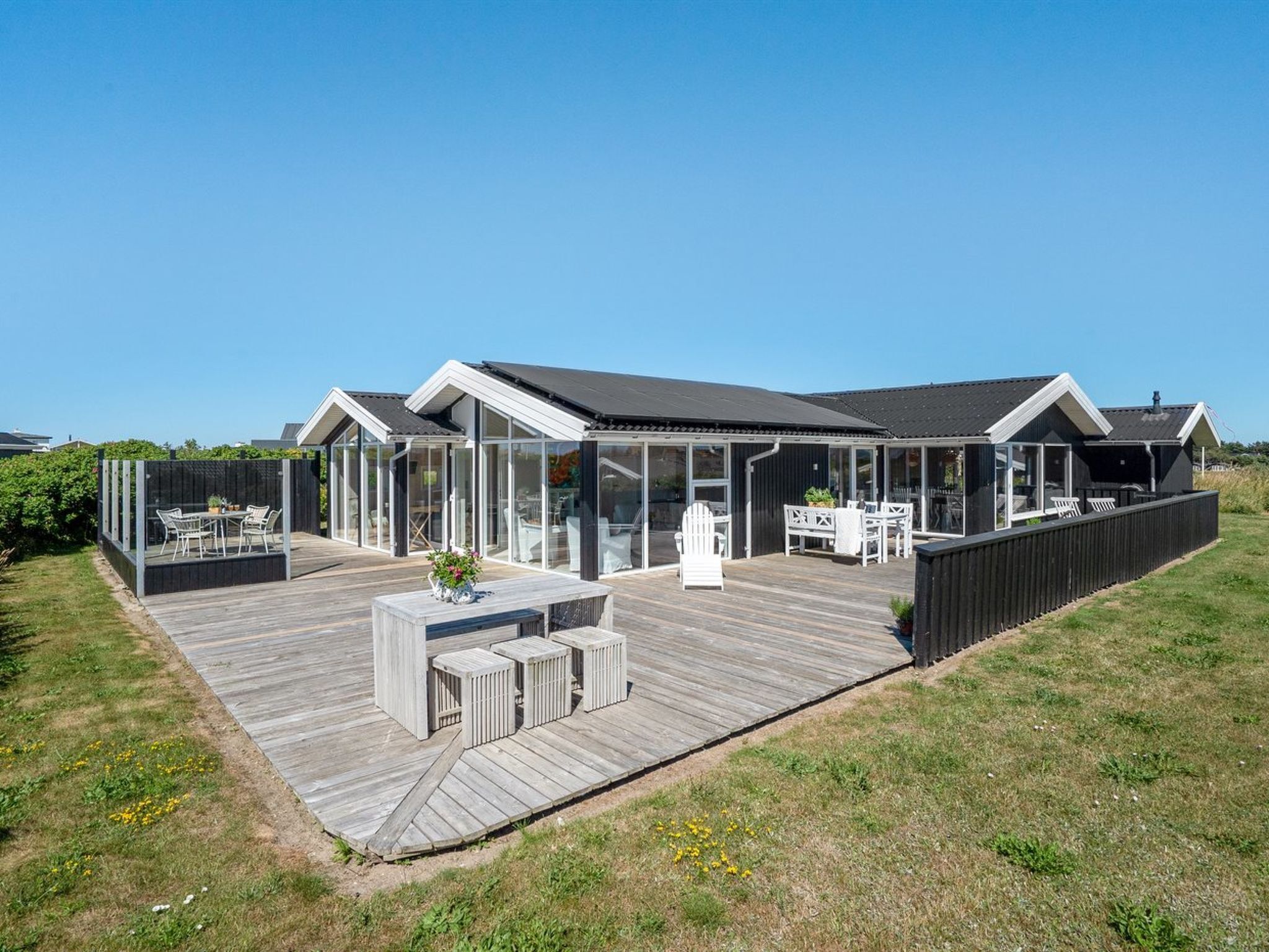 Et moderne hus med stor terrasse, glasafskærmning og udendørs møbler.