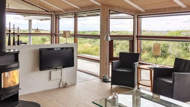 En moderne stue med pejs, et fladskærms-tv og store vinduer med udsigt til naturen.