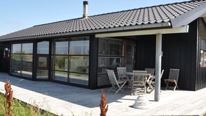 Et moderne hus med en stor glasudvidelse, udendørs siddepladser og en skorsten.