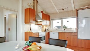 Une cuisine moderne avec des meubles en bois, un plan de travail blanc et une table à manger agrémentée d’un panier de fruits.