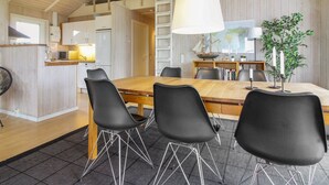 A spacious dining area with a wooden table and black chairs, a large white pendant light, and a bookshelf with books and a ship model.