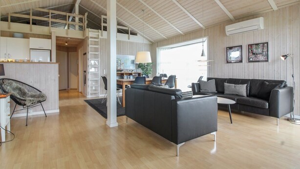 A spacious living area with a black sofa, a dining table, and a kitchen in the background.