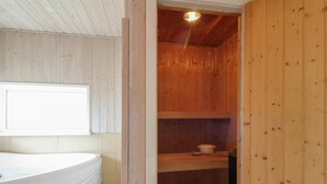 A sauna room with a wooden interior, a white bathtub, and a ceiling light.
