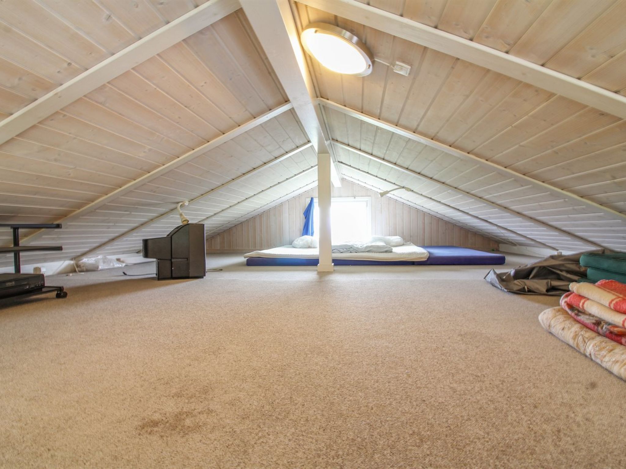 An attic bedroom with a sloped ceiling, a single bed, a desk, and a window.