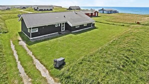 A modern house with a large garage and a satellite dish, surrounded by a grassy field and a body of water.