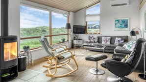 Una sala de estar moderna con una estufa de leña, un sofá, un sillón mecedora y un televisor.