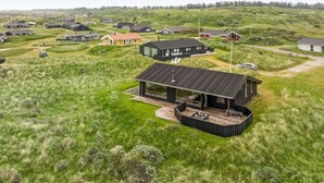 Una casa moderna con terraza, rodeada de un paisaje cubierto de césped y otras viviendas.