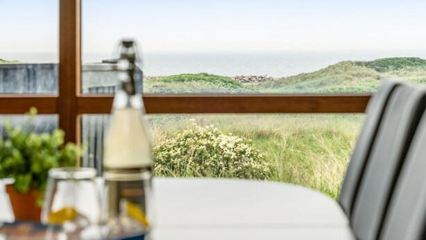 Una mesa de comedor con vistas al mar y colinas cubiertas de hierba.