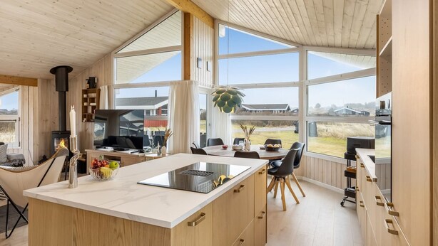 Eine moderne Küche mit einer großen Kochinsel, Holzschränken und großen Fenstern mit Blick auf die Landschaft.