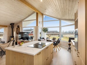 Una cocina moderna con una isla grande, armarios de madera y ventanas amplias que ofrecen vistas al campo.