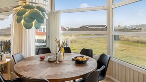 Ein runder Holztisch mit Stühlen, eine Zierleuchte und ein Blick ins Freie durch große Fenster.