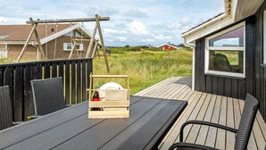 Une terrasse en bois avec une table et des chaises, une clôture en bois et, en arrière-plan, une vue sur des maisons et de la verdure.