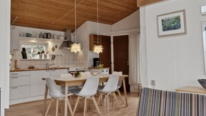 A modern kitchen with wooden cabinets, a dining area with a wooden table and chairs, and a ceiling with exposed beams.