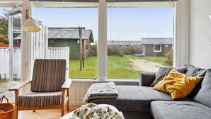A cozy room with a grey sofa, striped chair, and a view of a green house through large windows.