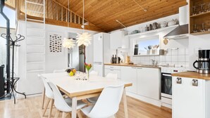 A modern kitchen with white cabinetry, wooden countertops, and a central island. There is a dining area with a white table and chairs, and a hanging light fixture above.