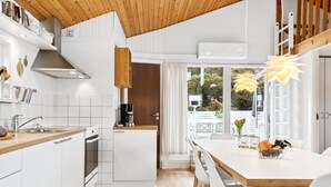 A modern kitchen with white cabinetry, wooden ceiling, and a dining area with a white table and chairs.
