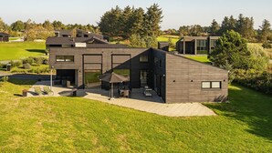 Une maison moderne à deux étages dotée d’un patio, d’un espace salon extérieur et offrant une vue sur le paysage environnant.
