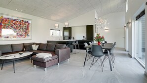 Un vaste espace de vie comprenant un canapé moderne, une table à manger avec des chaises et un grand tableau abstrait accroché au mur.