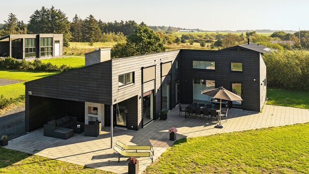 Une maison moderne dotée d’un patio, d’un espace salon extérieur et offrant une vue sur la campagne environnante.