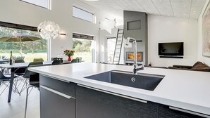 Une cuisine moderne dotée d’un grand îlot central, d’appareils électroménagers intégrés et d’un coin repas avec des sièges à l’extérieur.